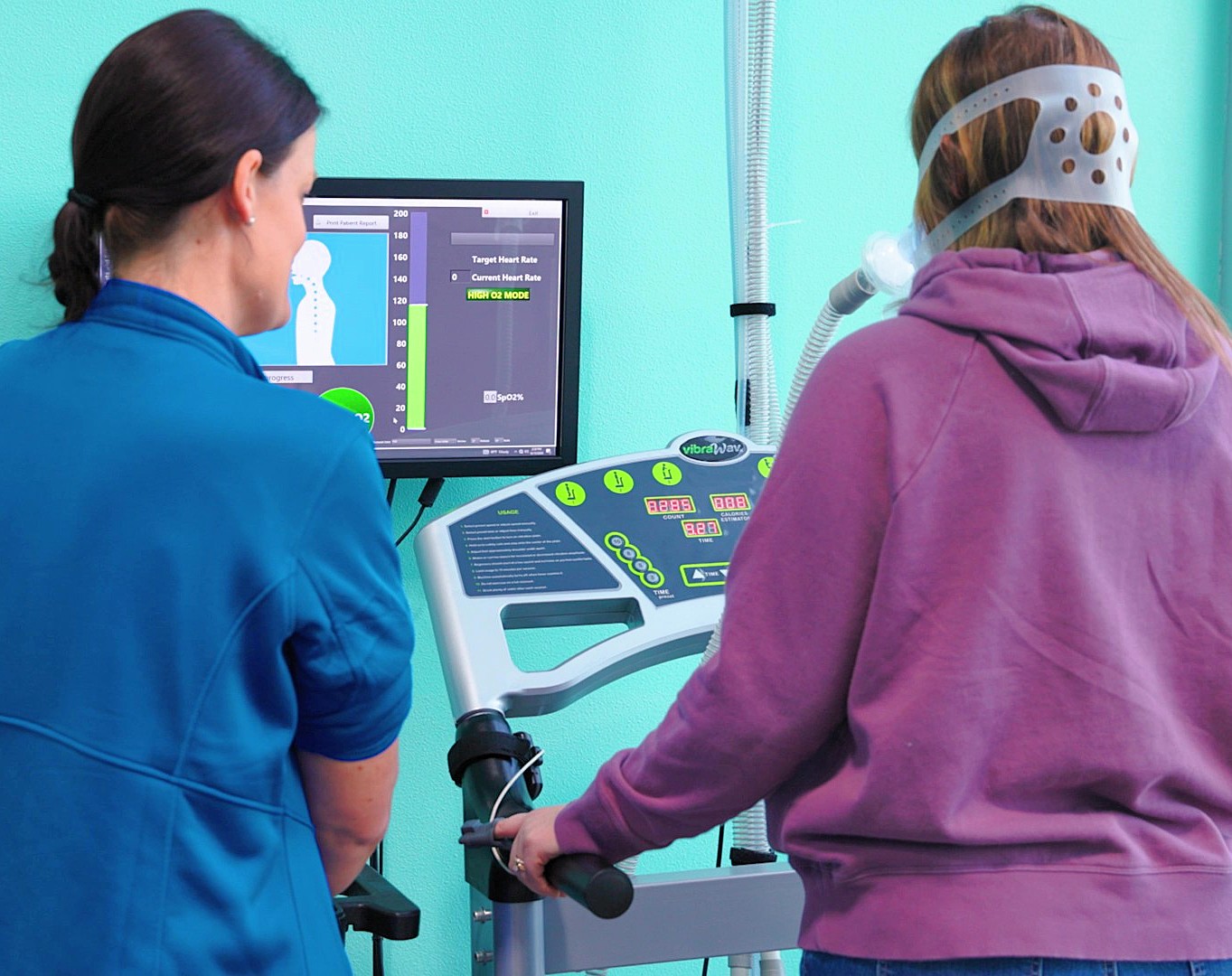 Nurse and patient standing together with their backs to the camera. The patient has a mask on and is receiving treatment for oxygen and ozone therapy near Cedar Rapids. The nurse stands by, monitoring the treatment.