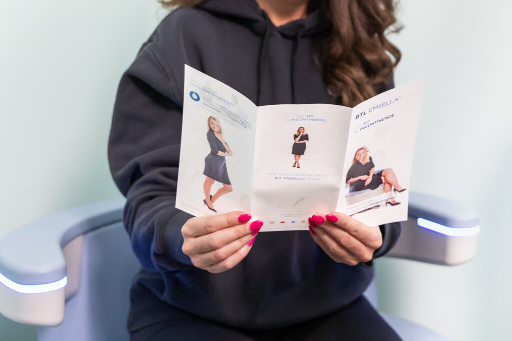 Woman sits on Emsella near Iowa City to strengthen her pelvic floor while reading an informational pamphlet about the chair.