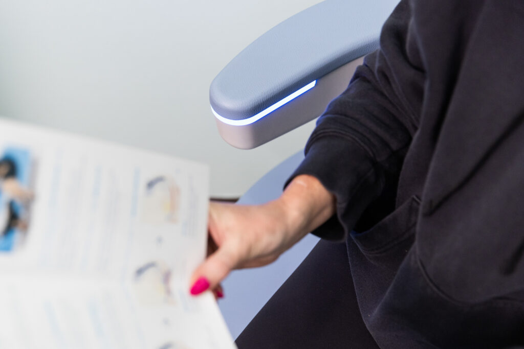 Woman sits on chair that serves as a urinary incontinence treatment in North liberty and reads a pamphlet that explains the function of the pelvic floor.
