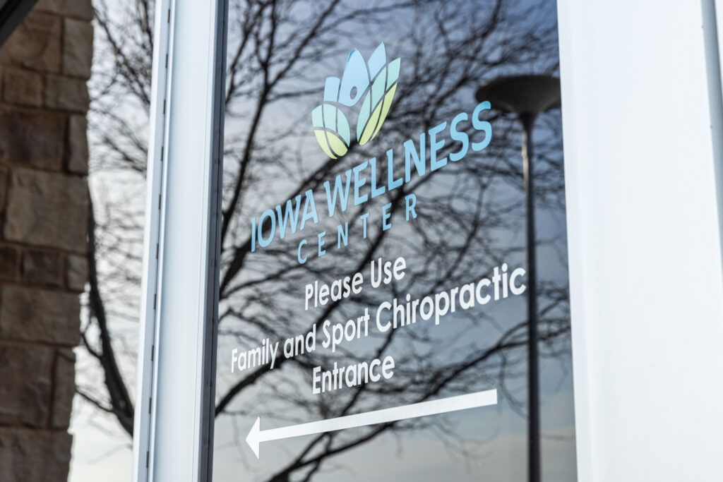 Door with the words 'Iowa Wellness Center' listed below a logo. Underneath the sign, there is additional text that says 'please use family and Sports Chiropractic entrance' with a sign pointing to the left. This is a wellness center where patients can receive treatments like ozone blood therapy near Cedar Rapids.