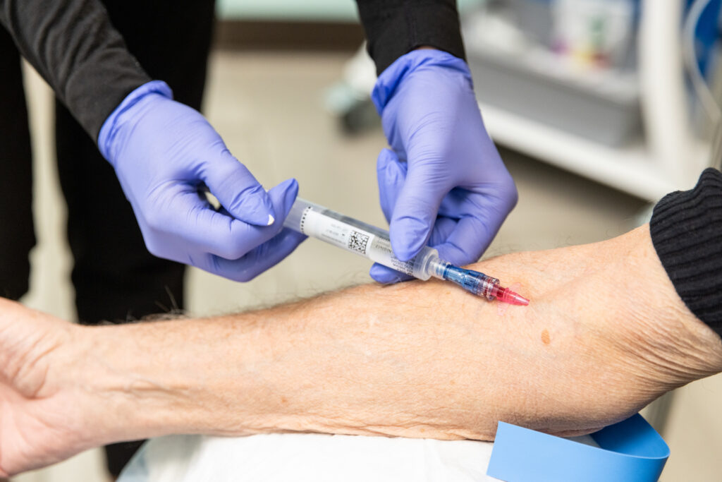 Closeup of provider holding syringe and inserting needle into the patient's arm for his IV therapy near Iowa City