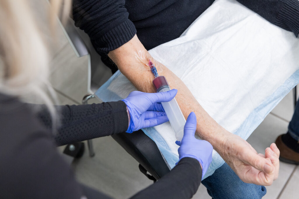 Nurse wearing gloves draws blood from patient's arm to cleanse it for ozone blood therapy near Cedar Rapids.