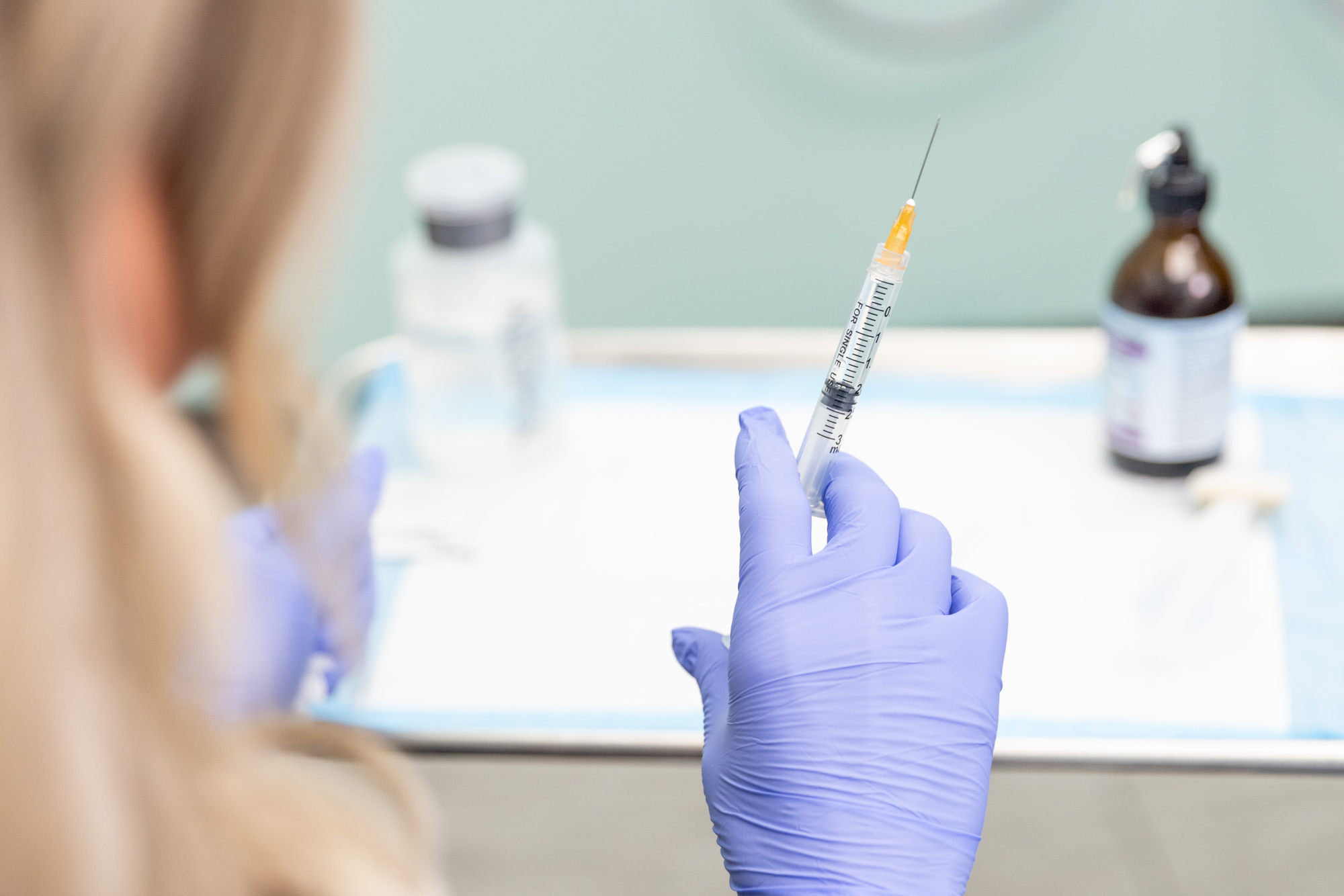 Woman wearing purple gloves holds syringe and prepares to treat patient with immune system dysfunction and chronic inflammation with regenerative medicine in North Liberty