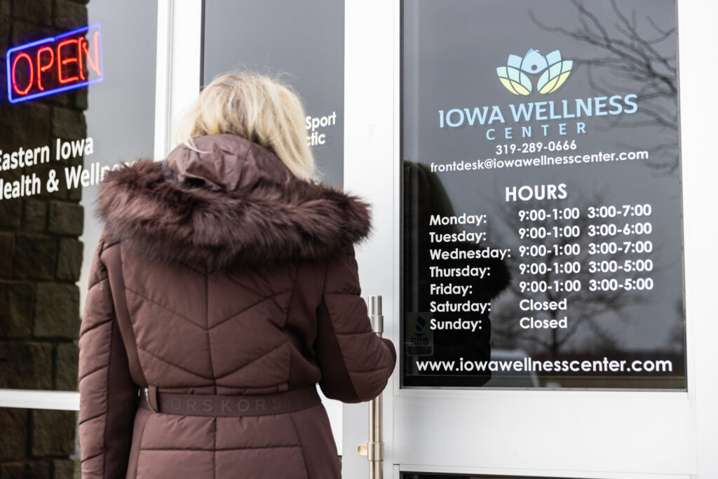 Woman wearing a big coat opens the door to Iowa Wellness Center to receive personalized care for her peripheral neuropathy treatment near Iowa City