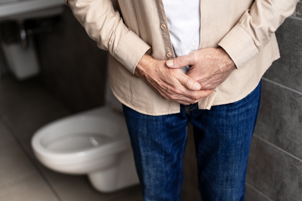 Senior man standing in bathroom and holding his hands in front of him, exhibiting signs of anxiety and embarrassment from not having the ability to control his bladder. This is an indication that he would benefit from urinary incontinence treatment in North Liberty.